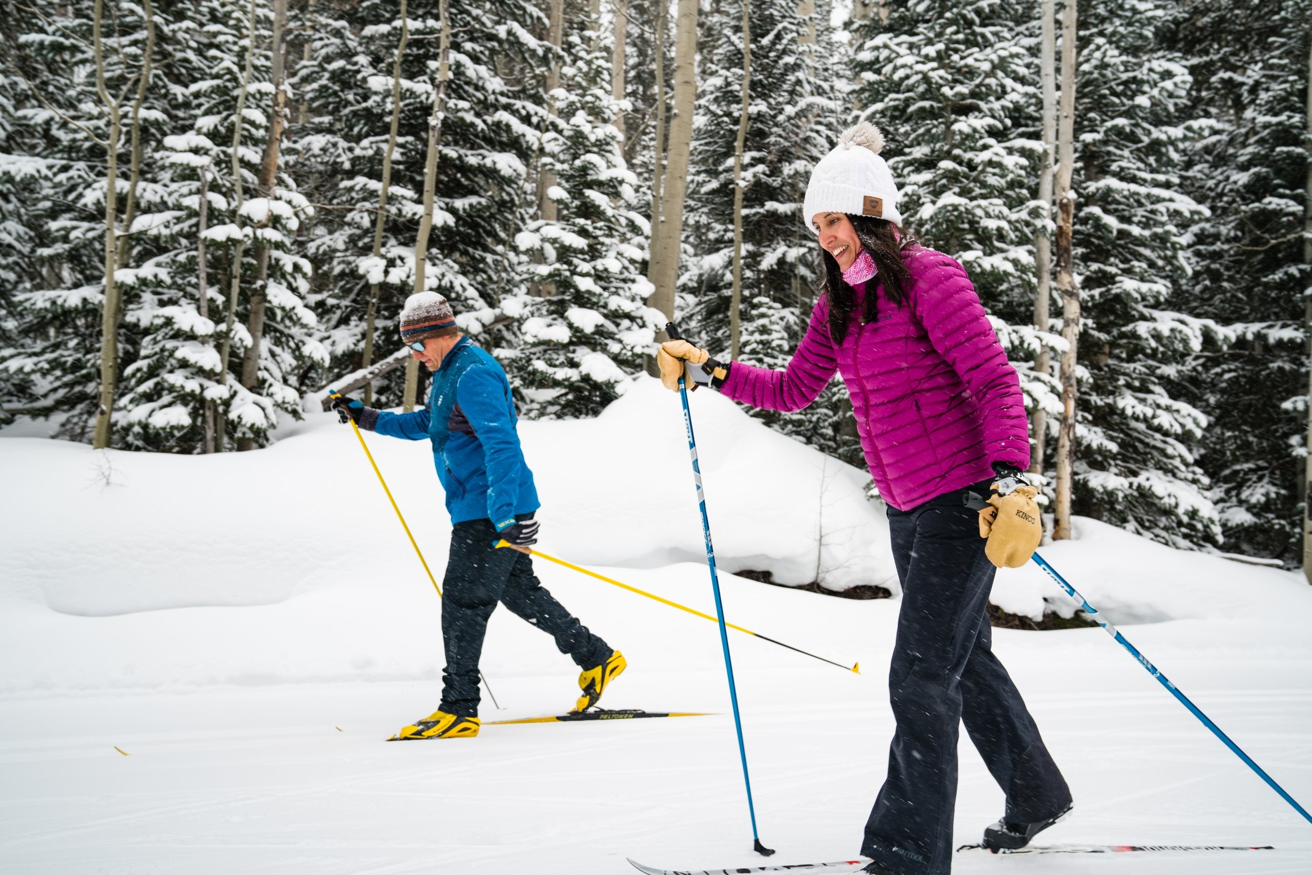 Middle aged skiers out for a ski through densely wooded forest.