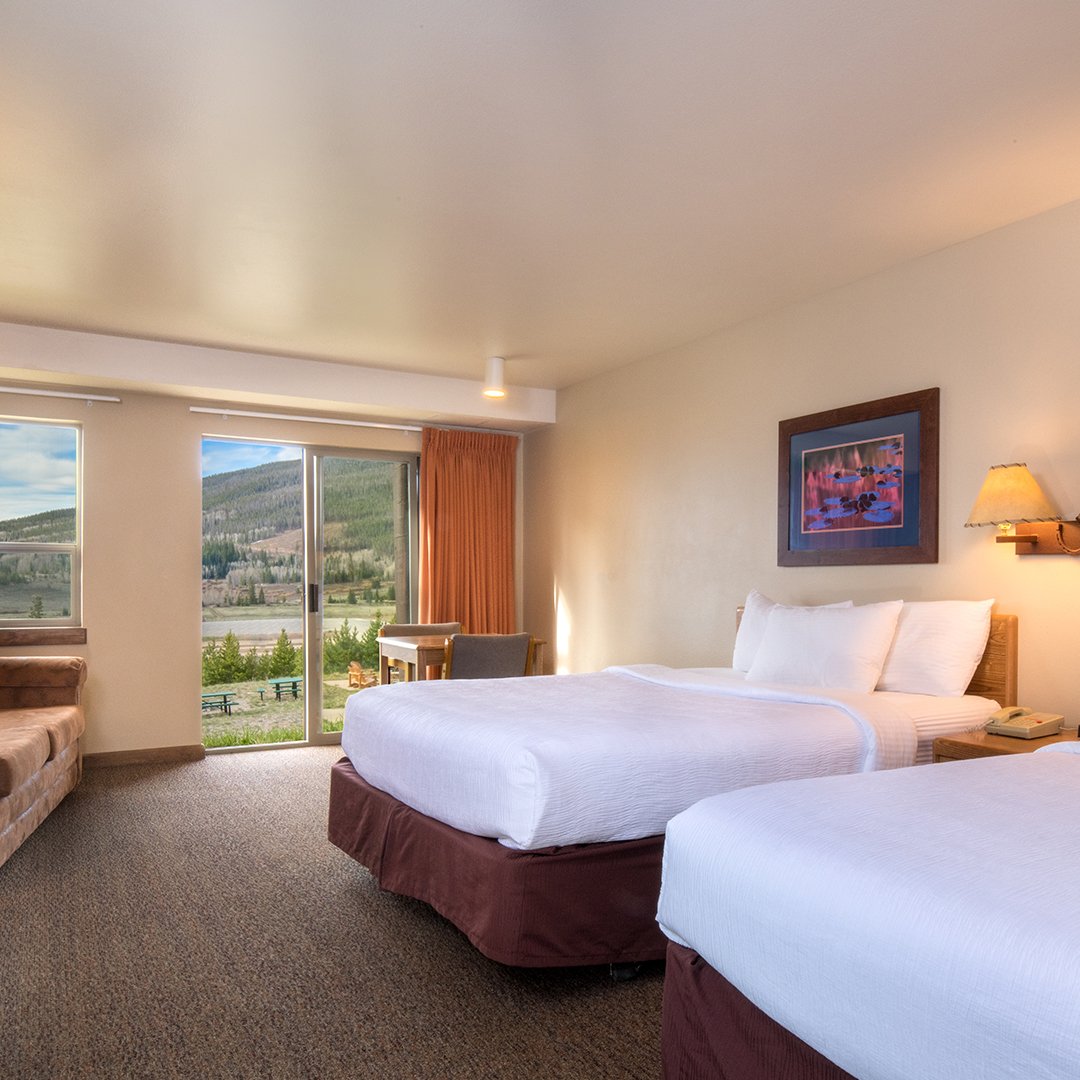 Clean, comfortable bedding with white sheets in a hotel room with a window looking out at a beautiful mountain landscape.