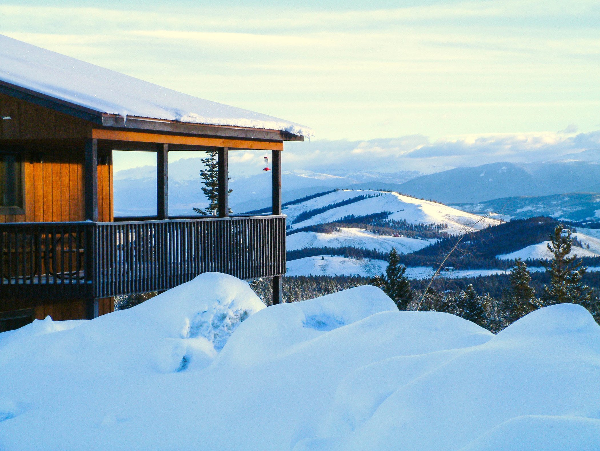 A winter cabin overlooking a valley and distant mountains covered in heavy snow