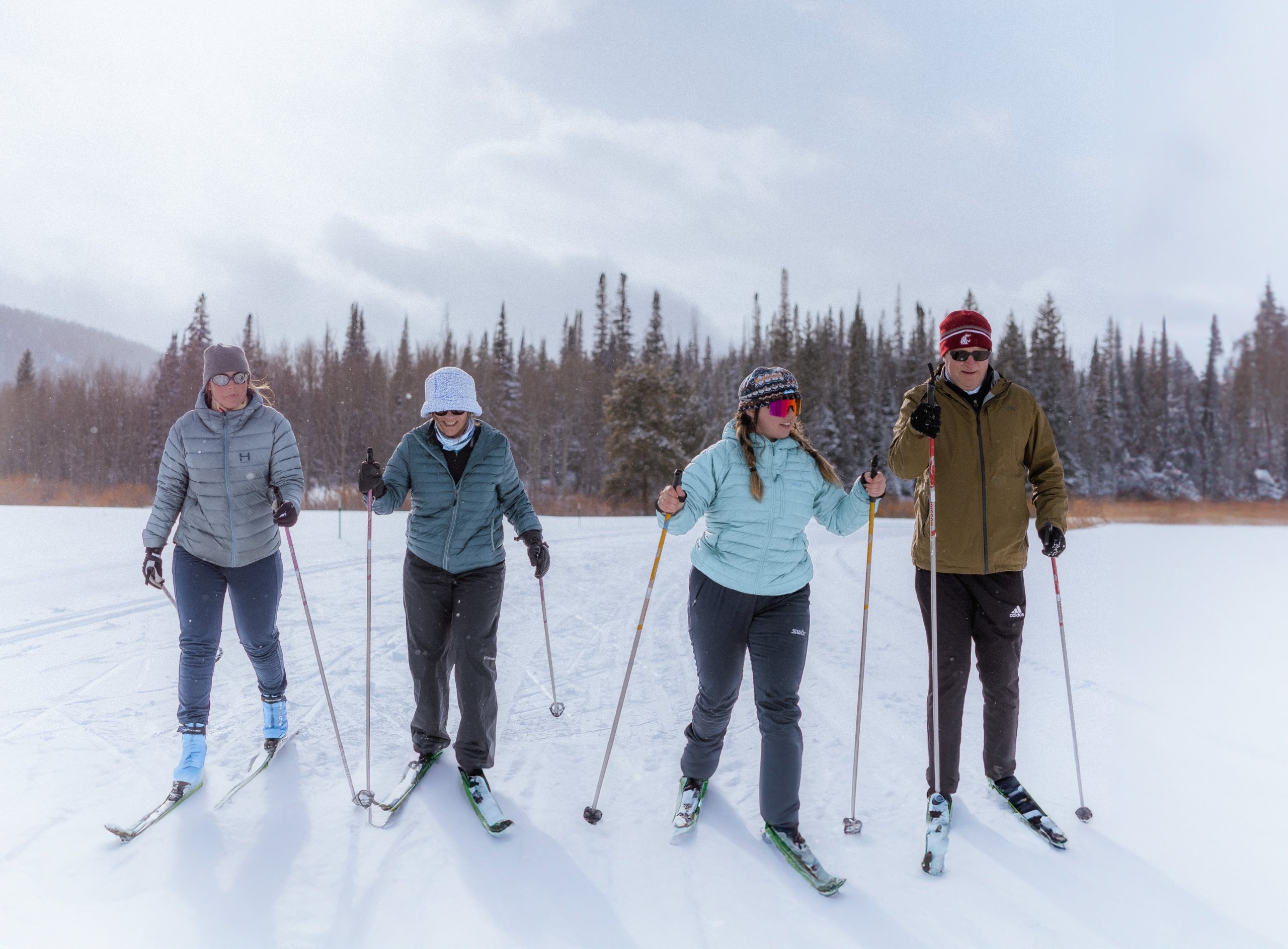 Group of 4 people cross country skiing in front of trees